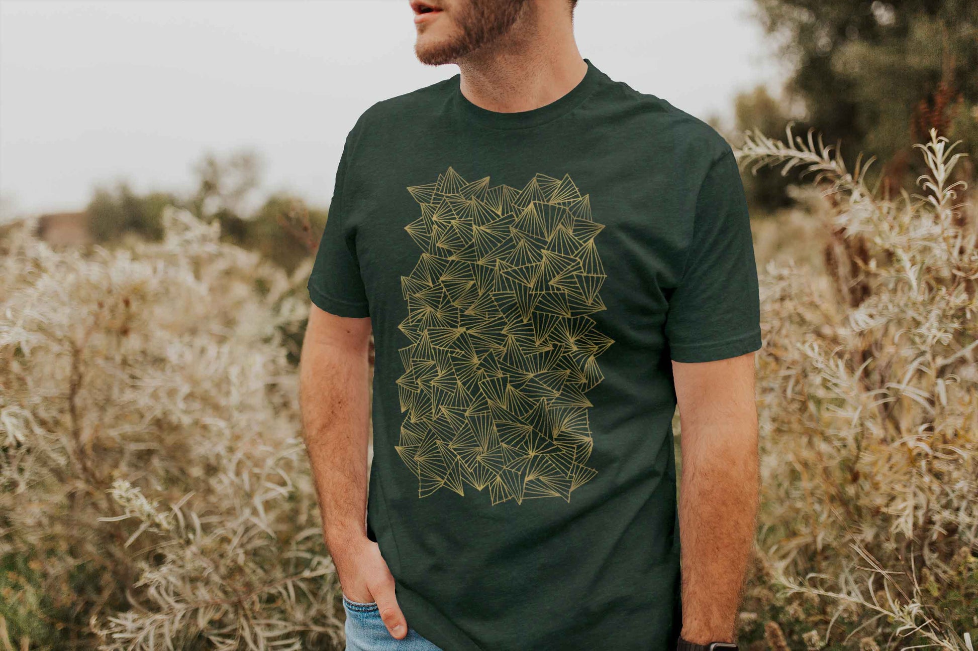 Model posing in a field with gaggle of triangles gold design on heather forest unisex t-shirt.